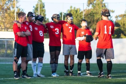 A group of blind soccer players on a field huddled up together