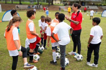 A group of youth soccer players is instructed by a coach