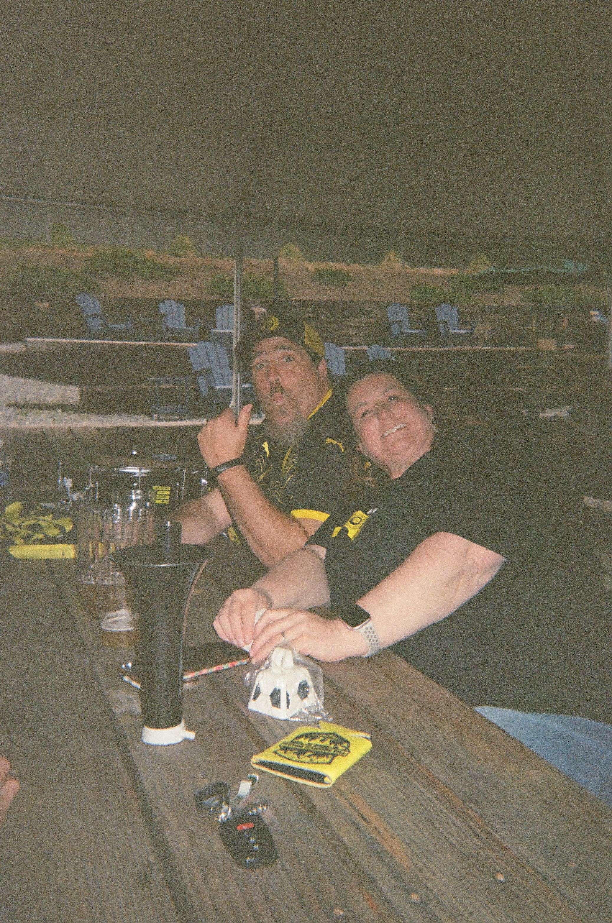 Two soccer supporters smile at a table with drinks and a drum nearby.