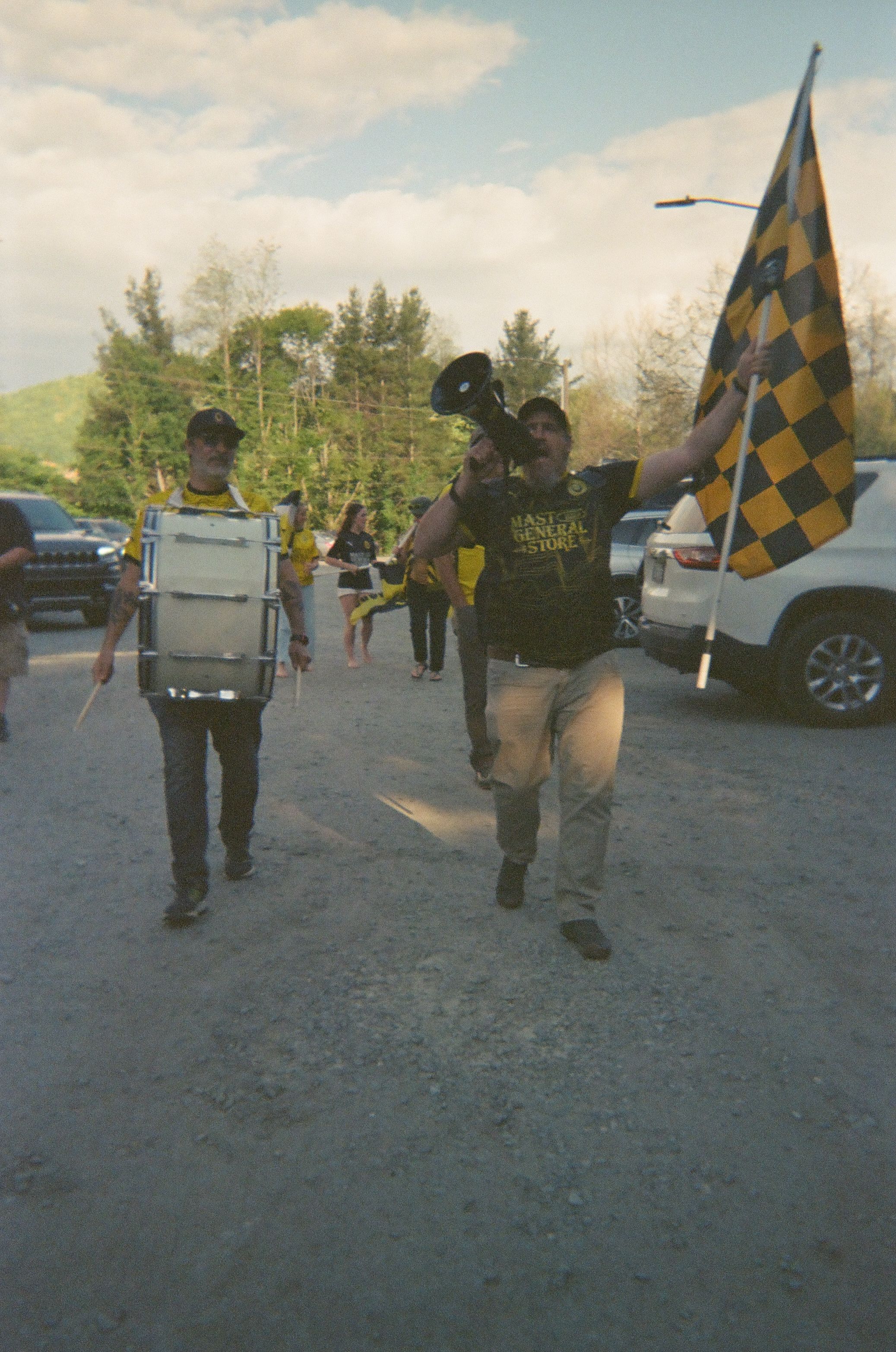Two soccer supporters march with a drum, megaphone, and yellow and black flag.