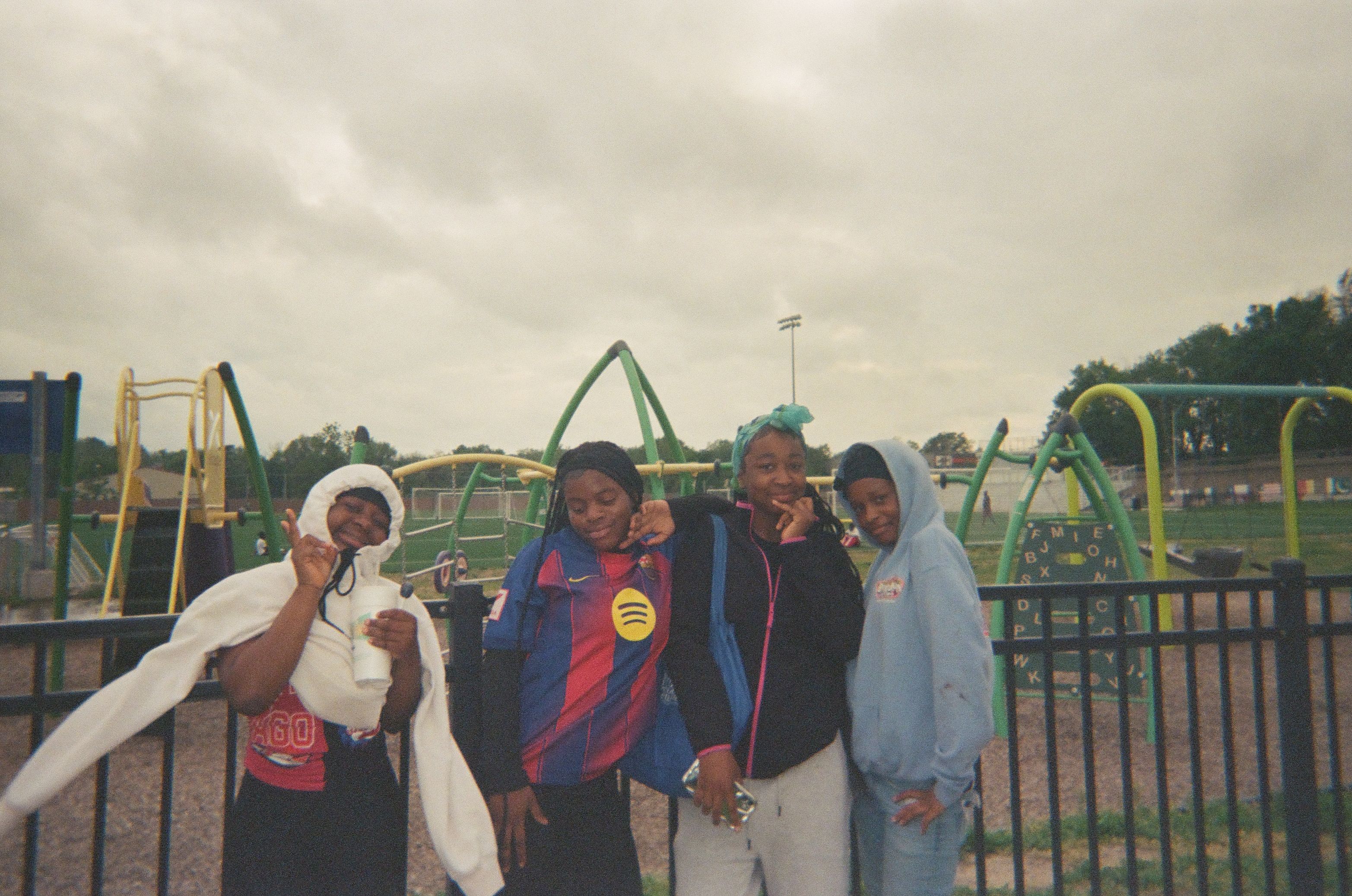 Four children stand together in front of a playground, smiling at the camera.