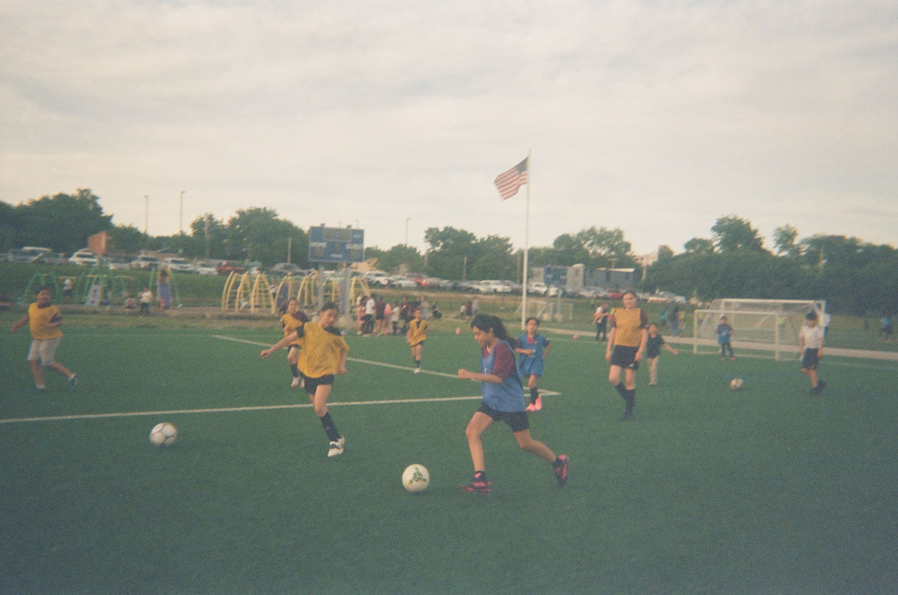 Children play soccer during a youth match on an outdoor field as families watch from the sidelines.