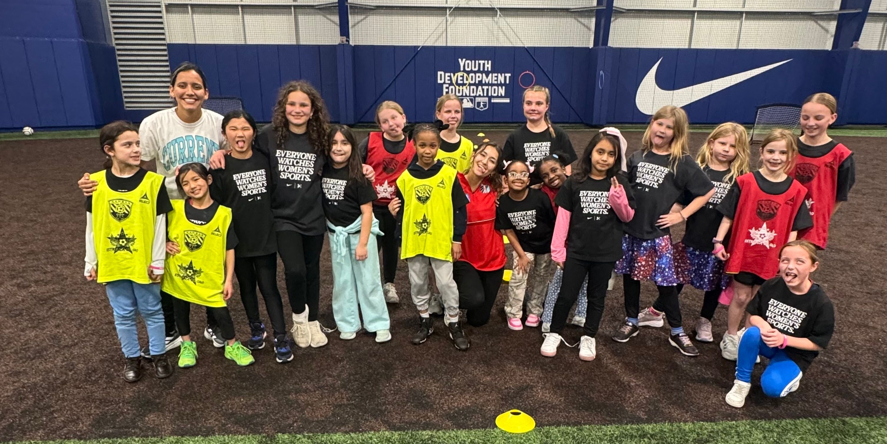 Children and coaches pose for a group photo during an indoor youth soccer session.