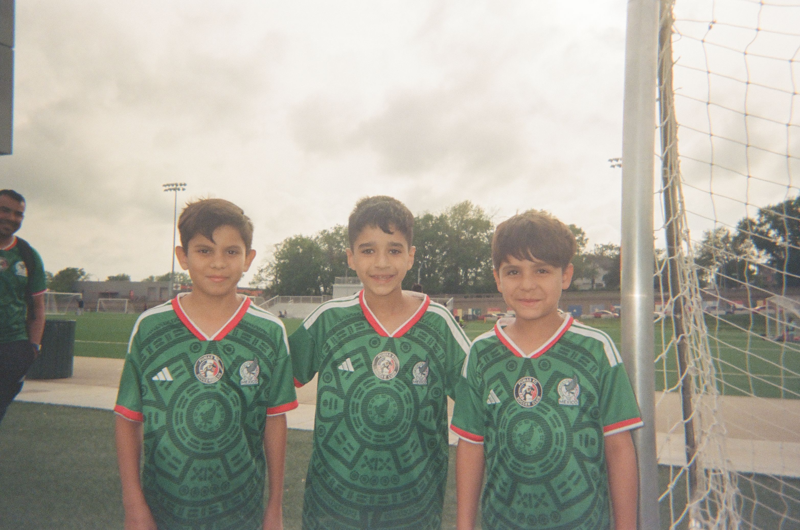 Three children wearing matching green soccer jerseys stand together on a soccer field.