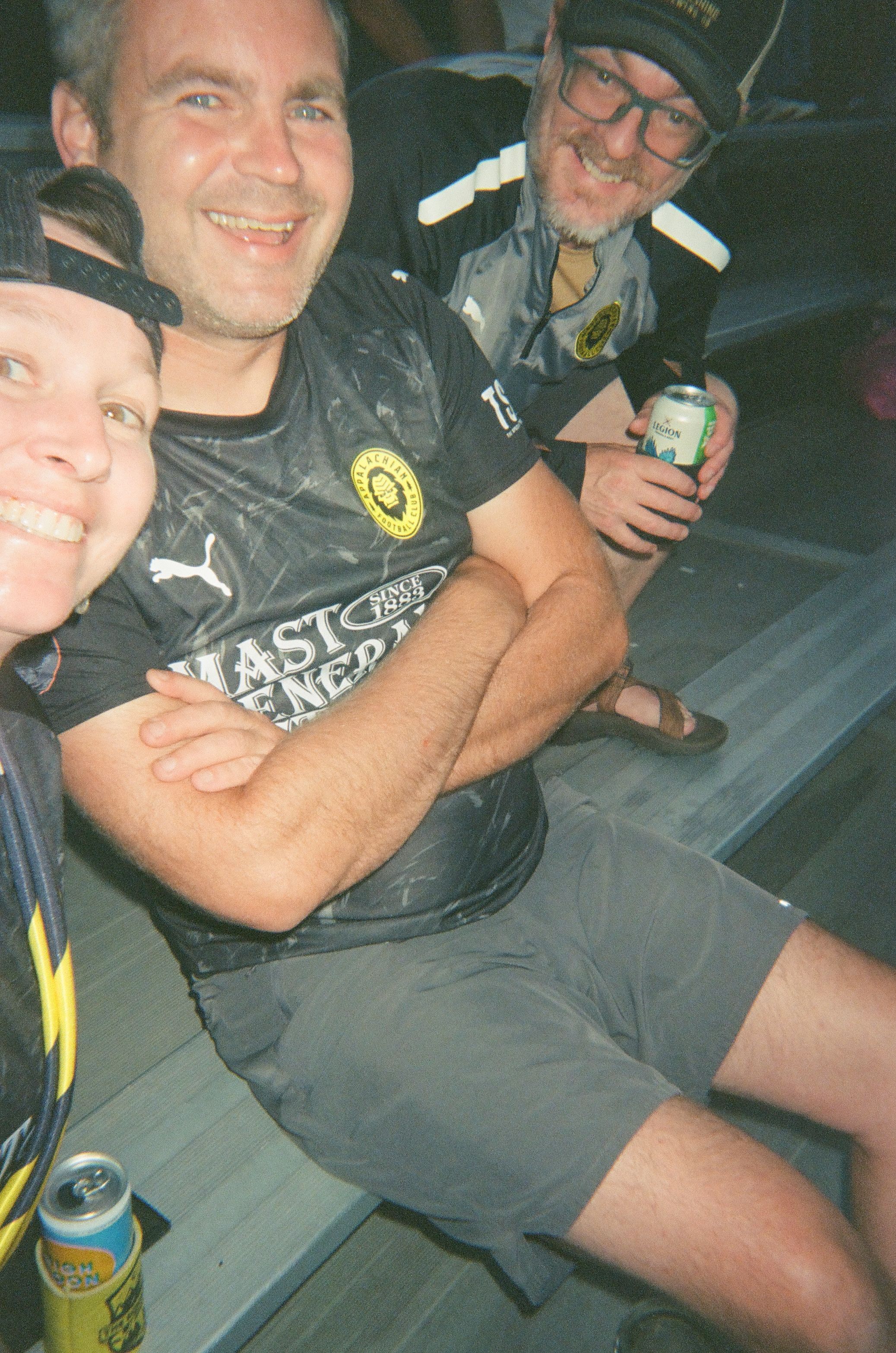 Three soccer supporters smile for a selfie in the bleachers.