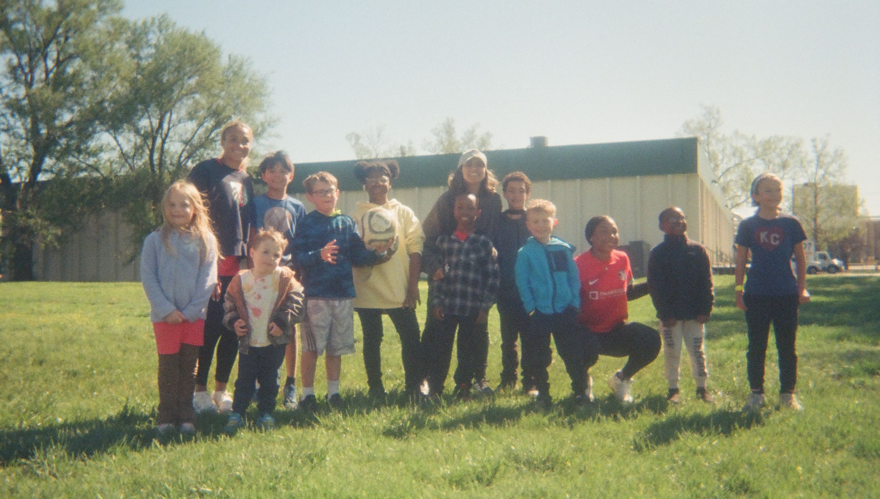 Group of children standing together on a grassy field outdoors.