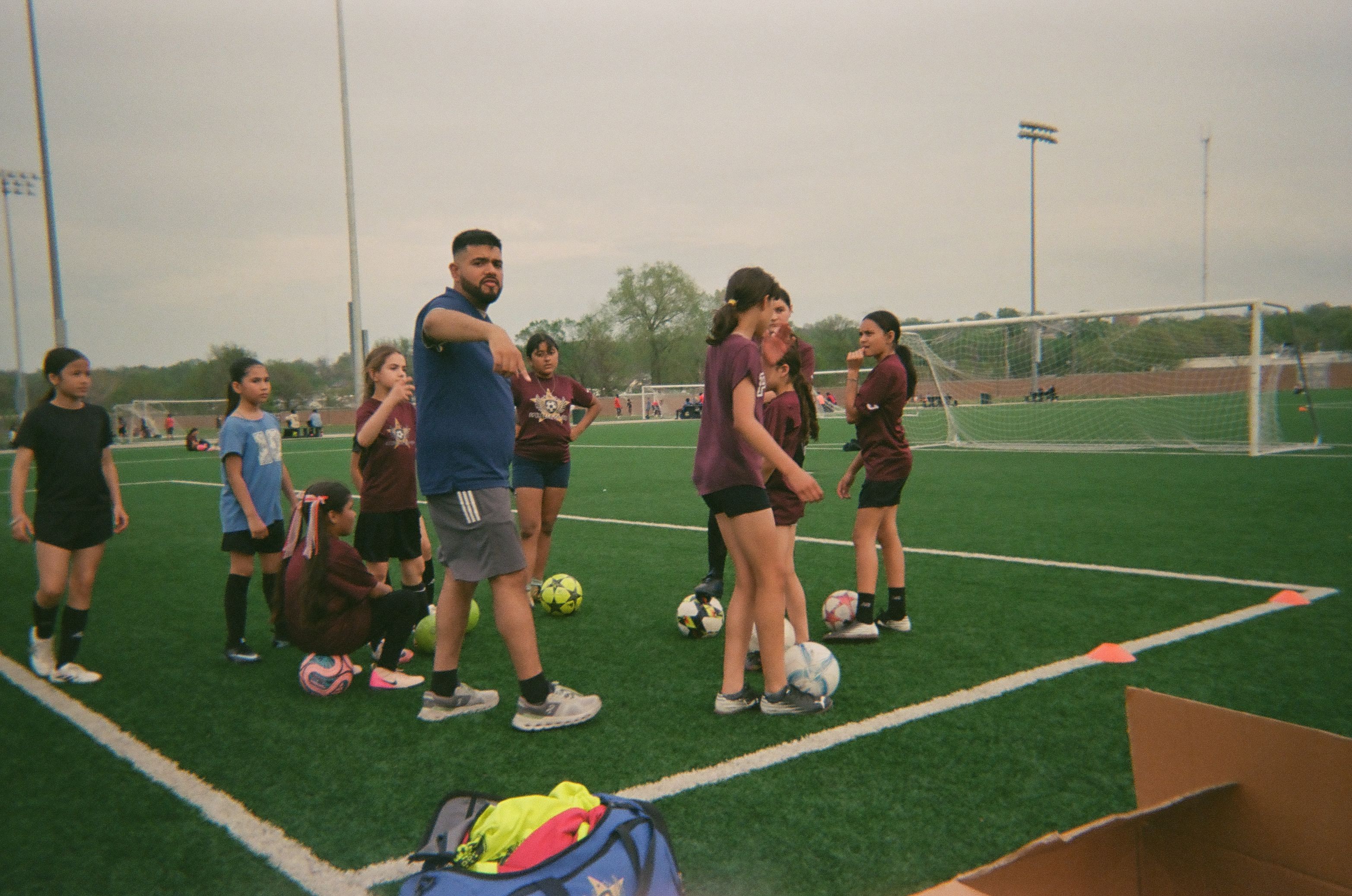 A coach leads a group of players through a training drill on an outdoor soccer field during a community training session.