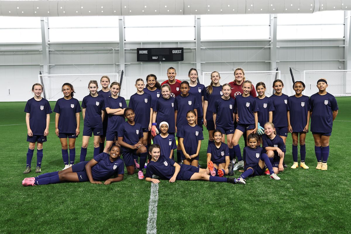 Youth soccer players and coaches pose together as a team on an indoor field.