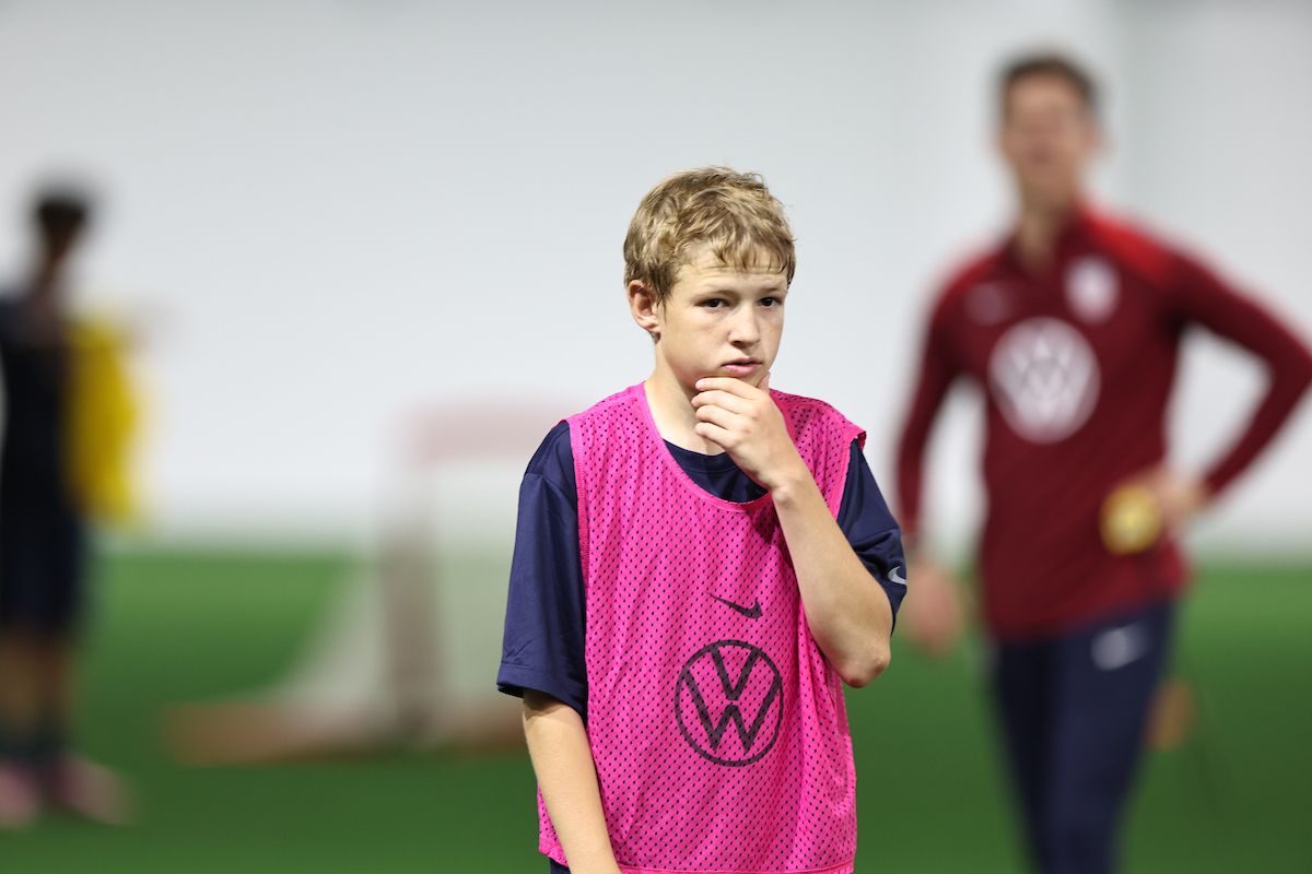Young player pauses thoughtfully, hand on chin, during a training session.