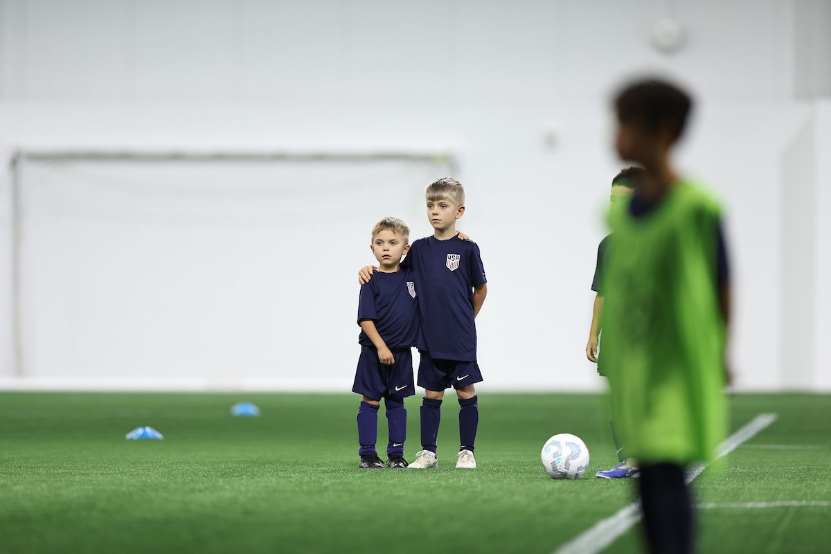 Two young players in U.S. Soccer kits stand together with arms around each other.
