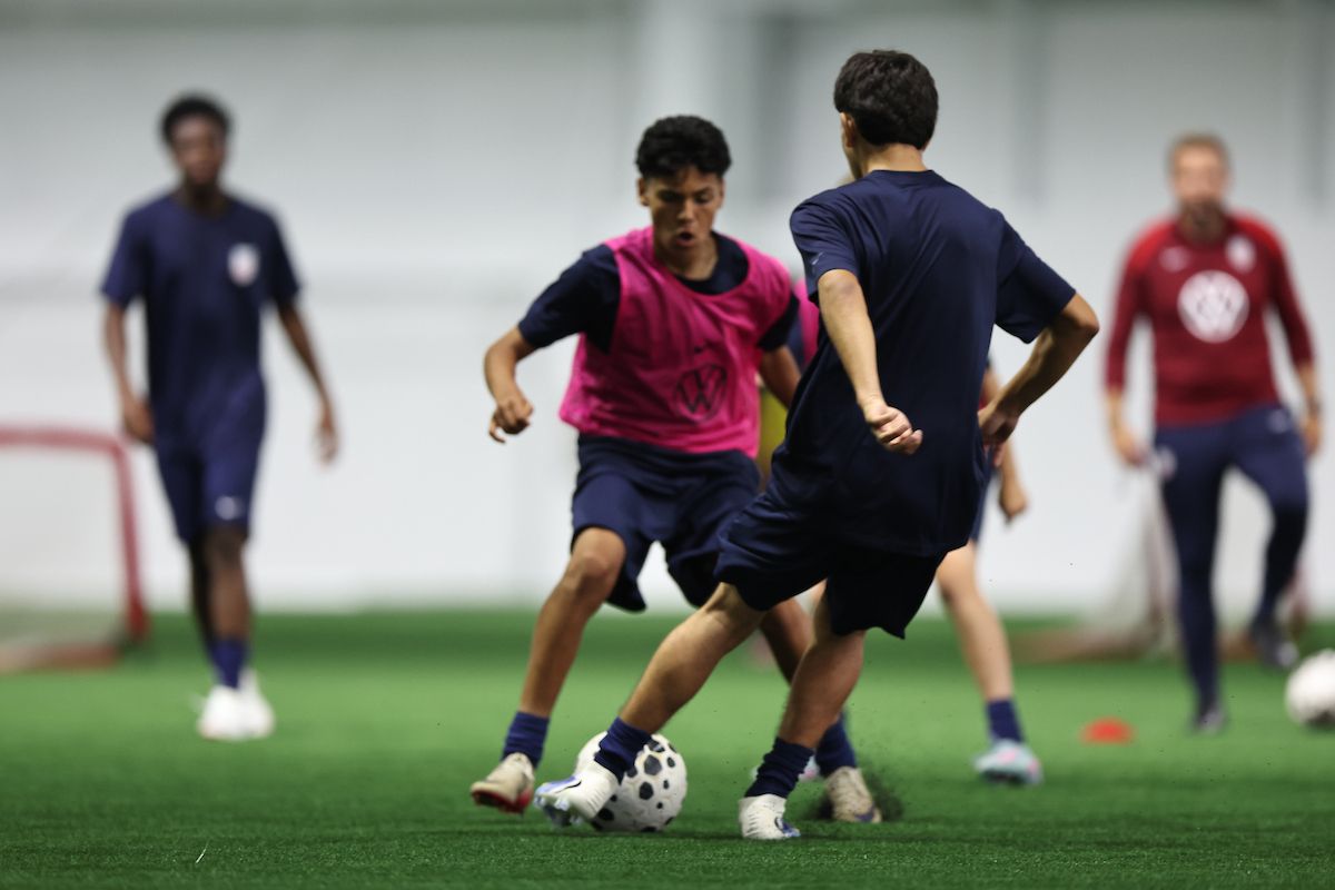 Young player dribbles past a defender during an indoor training session.