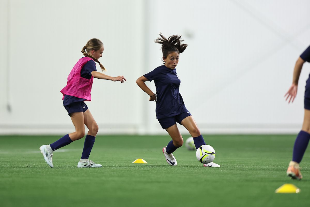 Young player dribbles past a defender during an indoor training drill.