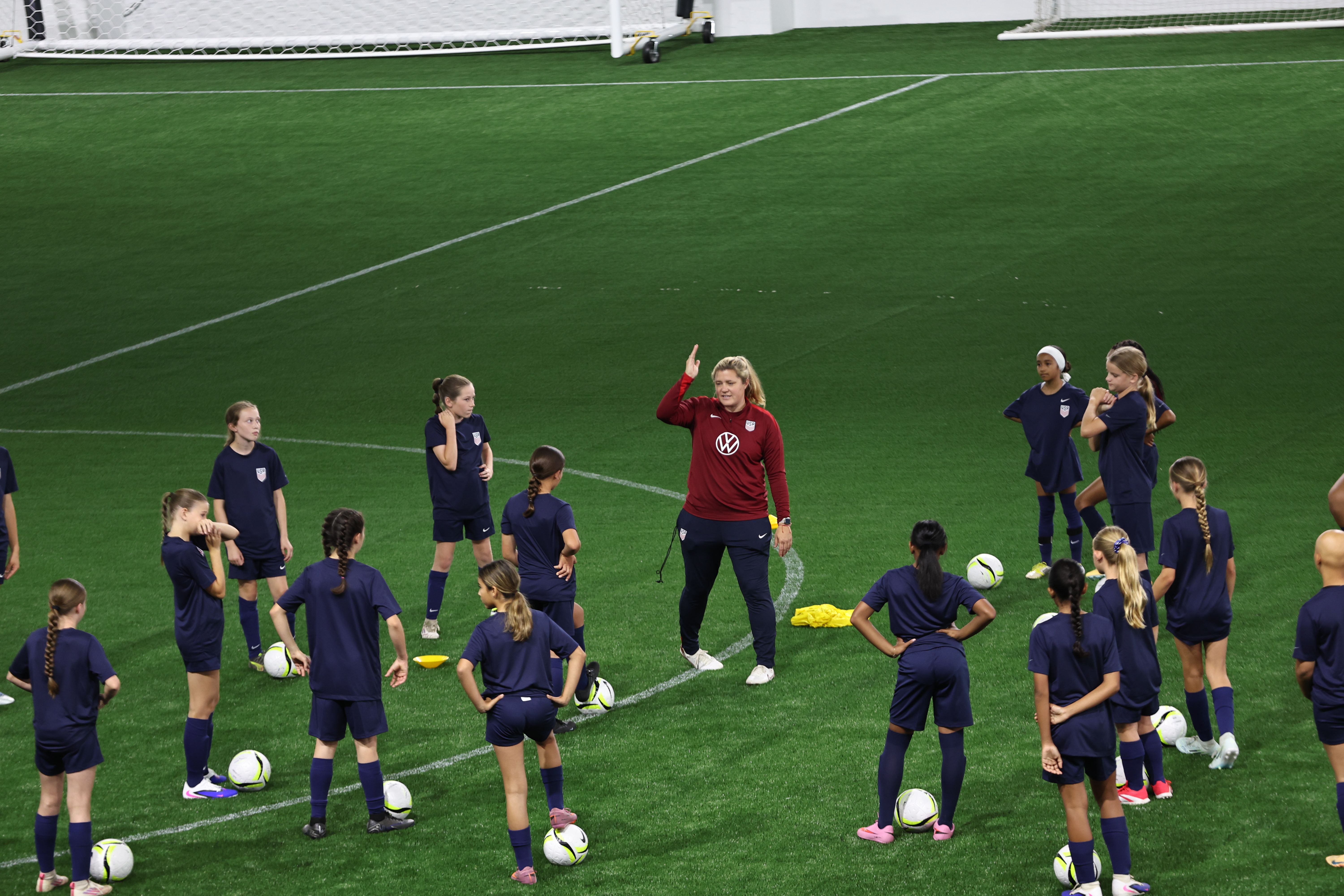 U.S. Soccer coach crouching to address a group of young players at training