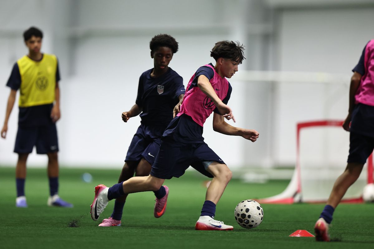 Youth player shields the ball from a defender during an indoor training session.