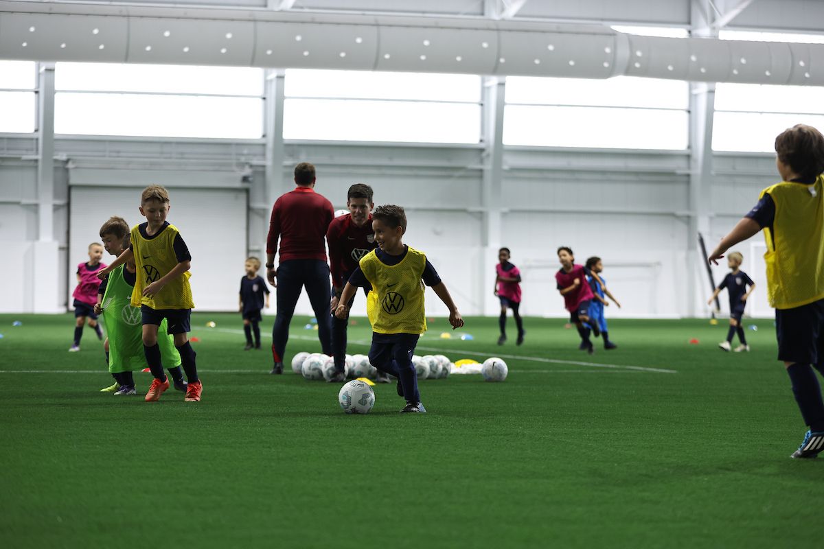 Young children dribbling soccer balls during a youth training session.