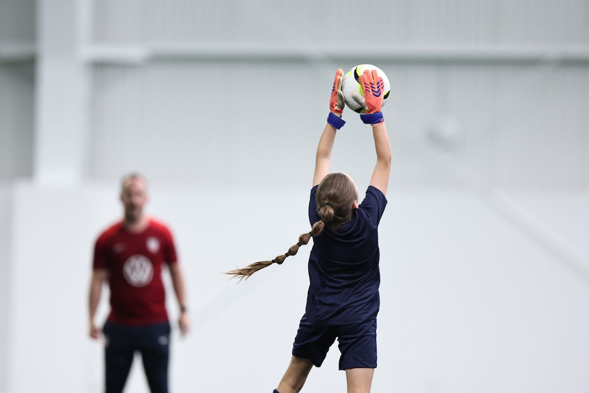 Young goalkeeper catches ball at full stretch during indoor training session.