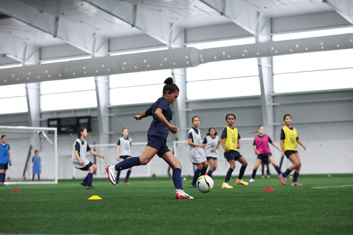 Young girl dribbles a soccer ball during a youth training session indoors.