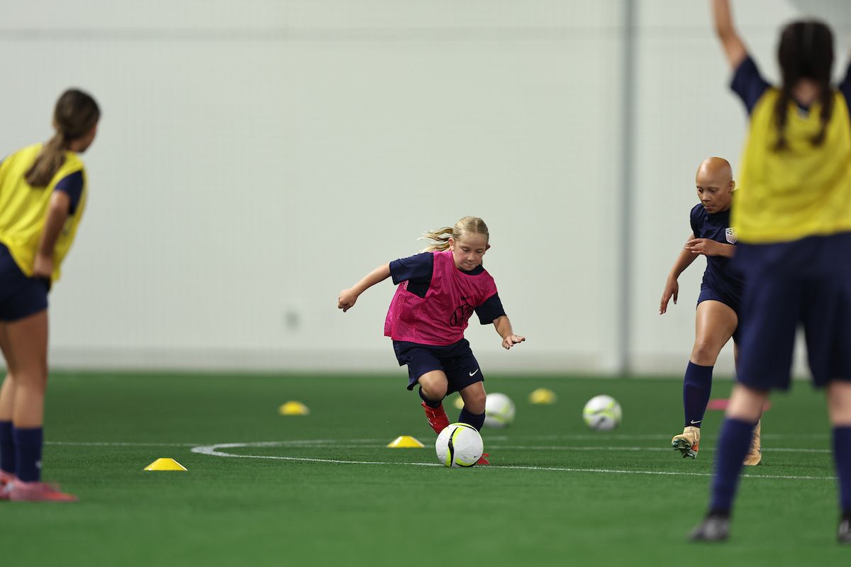 Young girl dribbling a soccer ball during a training drill with other players