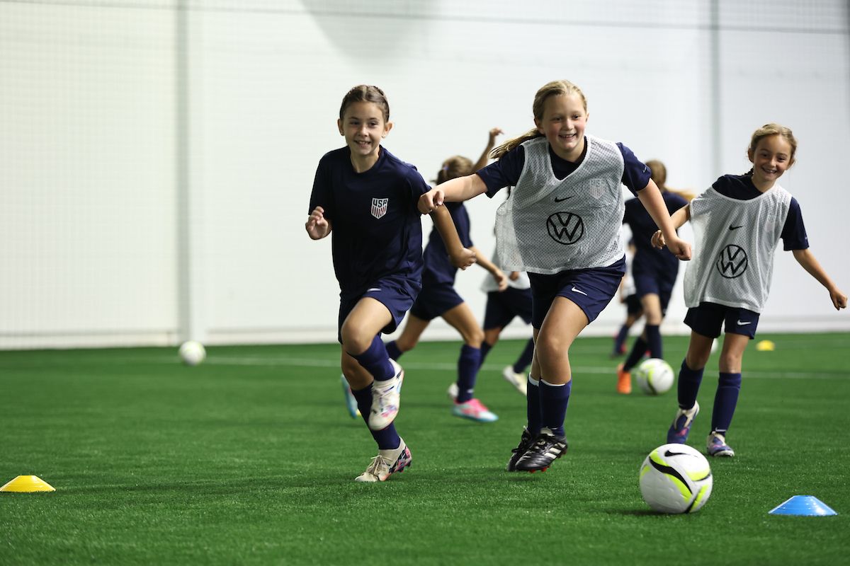 Young girls laughing and running during a soccer training session.