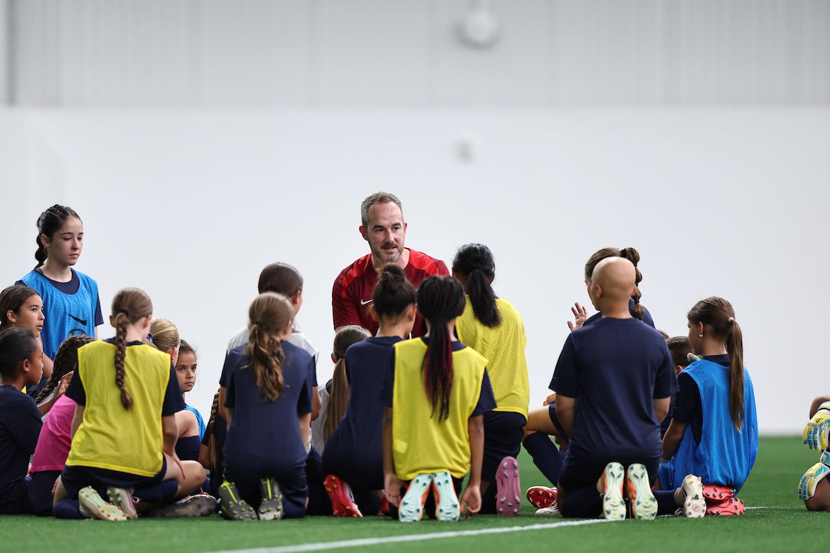 Coach kneeling and talking with a group of young female soccer players